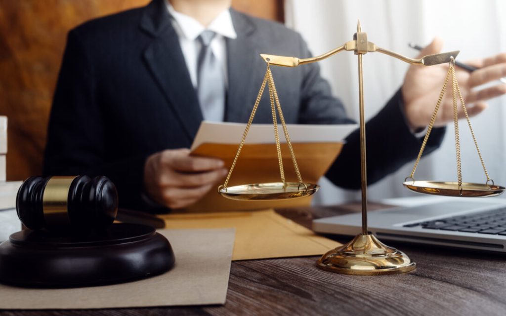 Justice and law concept.Male judge in a courtroom with the gavel, working with, computer and docking keyboard, eyeglasses, on table in morning light